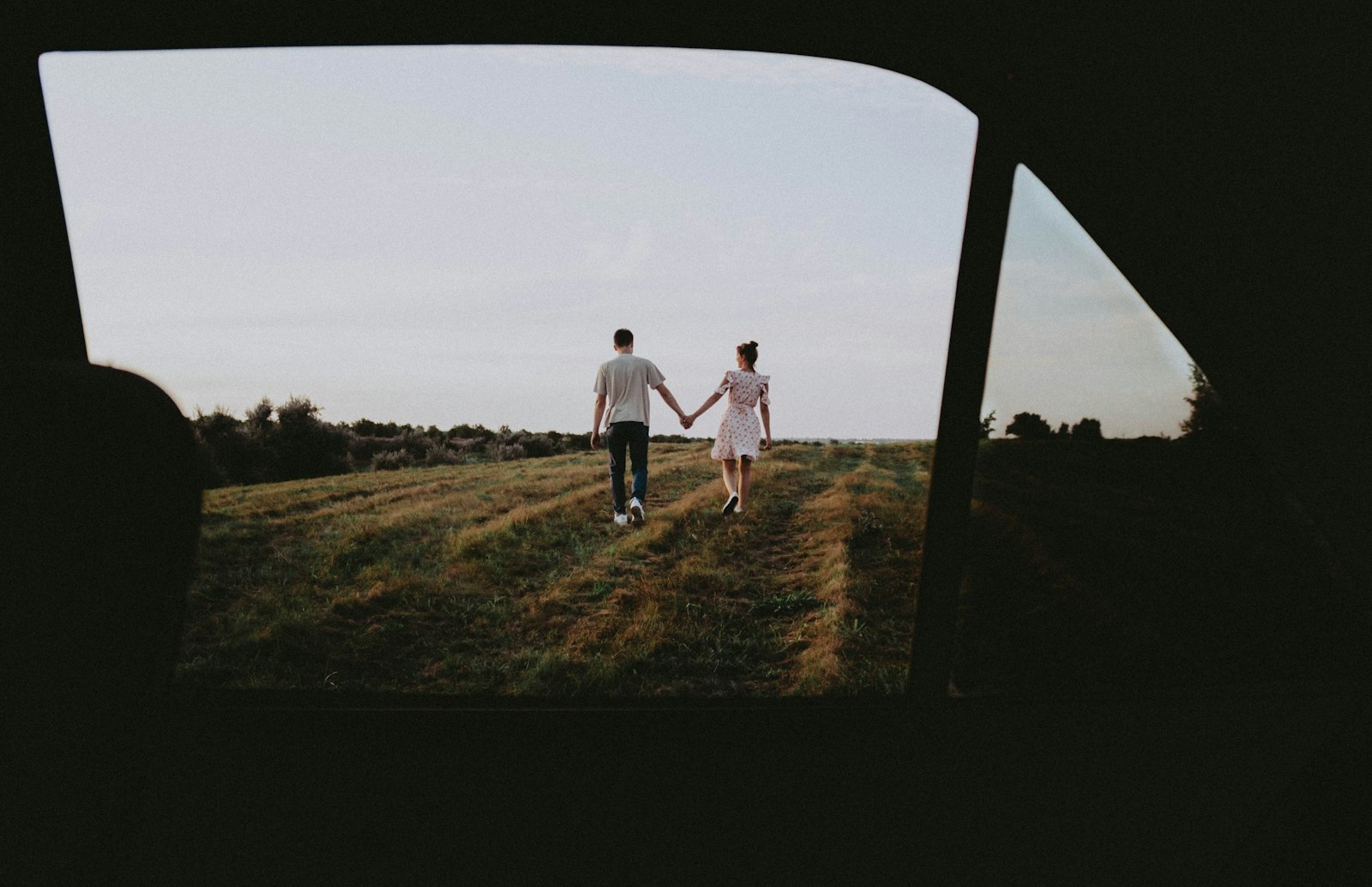 A couple walking hand in hand across an open field at dusk, seen from behind
